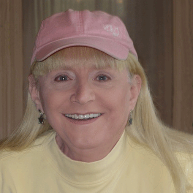 old lady wearing yellow turtle neck and pink ball cap